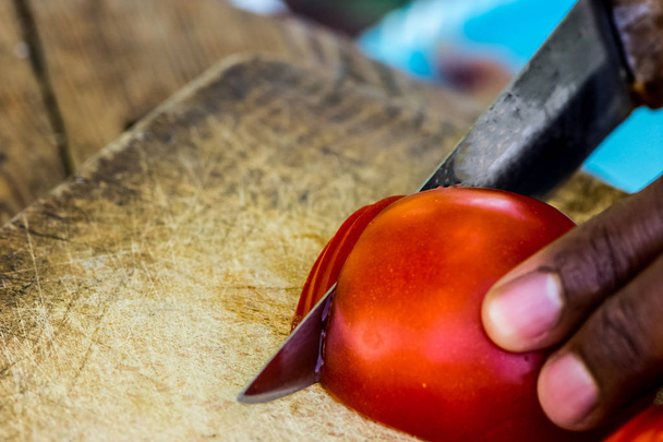 Человек режет помидоры на ломтиках старого деревянного стола, готовясь к обеду.
 - Фото, изображение
