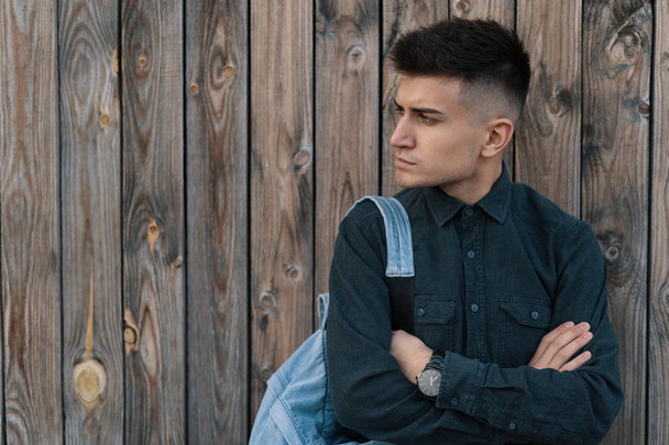 Молодой стильный студент позирует с джинсовым рюкзаком на деревянном фоне с копировальным пространством
. - Фото, изображение
