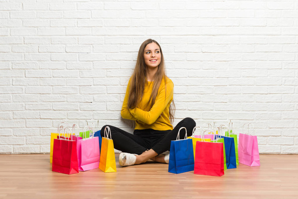Chica joven con un montón de bolsas de compras mirando por encima del hombro con una sonrisa
 - Foto, Imagen