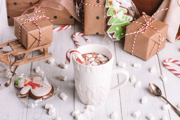 Cup of cocoa or chocolate on wooden Christmas background. Winter hot chocolate drink with marshmallows, snowman and a fir-tree cookies, candy canes - Photo, Image