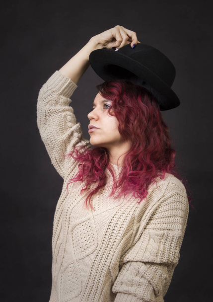 Emotional brunette in a hat and sweater with long hair posing in the Studio.Isolated images on a dark background. - Fotografie, Obrázek