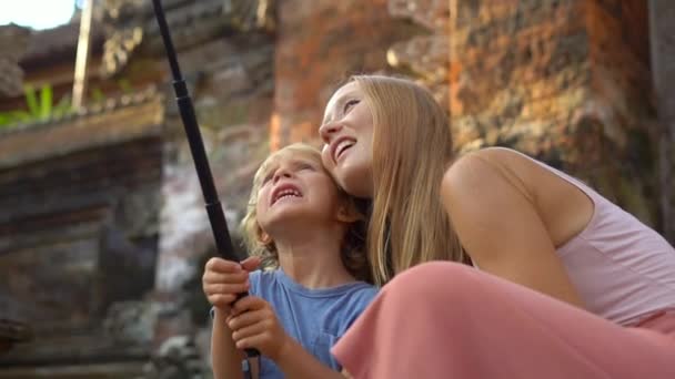 Slowmotion prise d'une belle jeune femme et son petit fils font un selfie avec une caméra d'action sur les escaliers du temple balinais. Voyage en Indonésie concept. Concept Voyage avec enfants
 - Séquence, vidéo