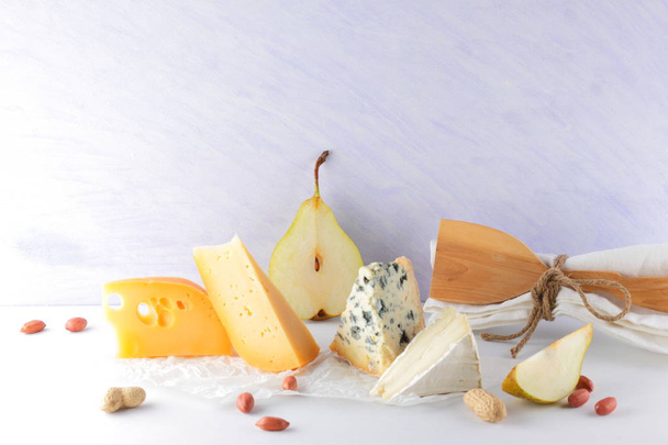 Various cheeses, pears and peanuts on white background. Blue cheese and camembert on parchment paper. Dairy products and fruits for breakfast. Healthy food. Copy space - Foto, imagen