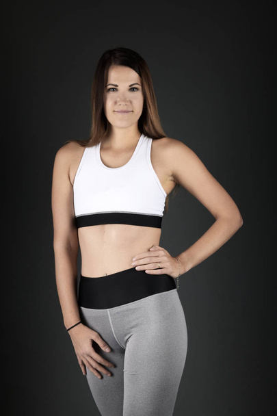 Young fitness woman in sports clothing on black background - Фото, изображение