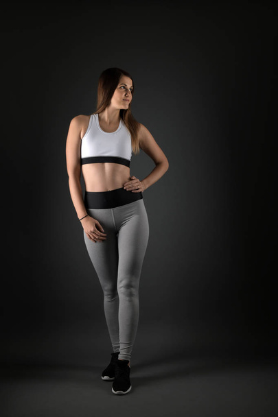 Young fitness woman in sports clothing on black background - Foto, Imagen