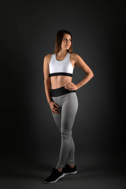 Jonge fitnessvrouw in sportkleding op zwarte achtergrond - Foto, afbeelding