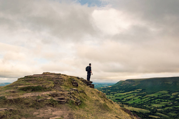 A man with a rucksack looking across the landscape of fields and hills from the top of a hill on the English, Welsh border. Black Mountains, Wales.  - Photo, image