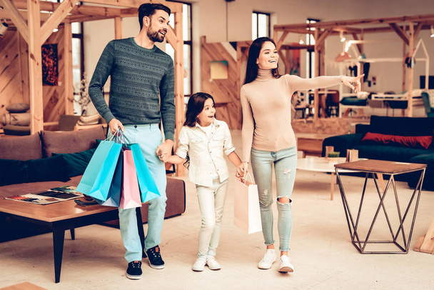 Young Smiling Family With Purchase Bags. Furniture Store Concept. Sunny Day. Good Mood. Loving Each Other. Bright Light. Happy Together. Going Shopping. Look At The Couch. Different Colors. - Fotó, kép