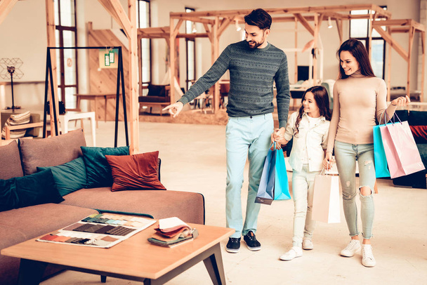 Young Smiling Family With Purchase Bags. Furniture Store Concept. Sunny Day. Good Mood. Loving Each Other. Bright Light. Happy Together. Going Shopping. Look At The Couch. Different Colors. - Foto, imagen