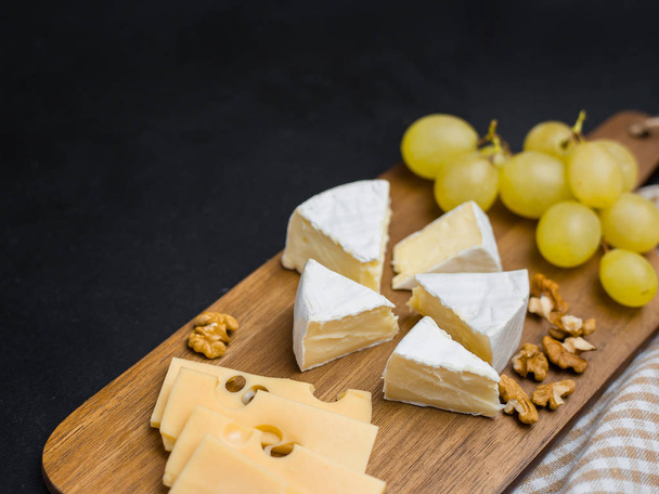 Rebanada de queso, nueces y uvas en tabla de cortar de madera. Queso Camembert y queso edam. Comida para el vino y romántico
 - Foto, imagen