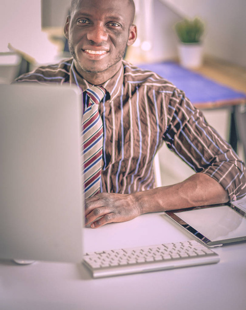Handsome afro american businessman in classic suit is using a laptop and smiling while working in office - Foto, immagini