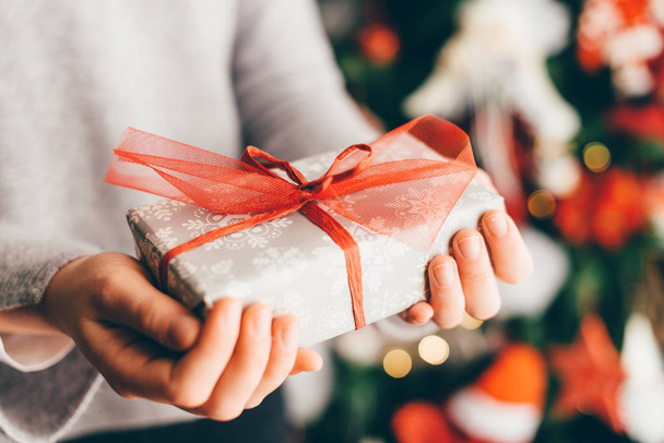 Close view of woman hands holding Christmas present on blurry Christmas tree background  - Photo, Image