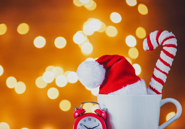 White cup of tea or coffee and alarm clock on Christmas Lights on background - Photo, Image