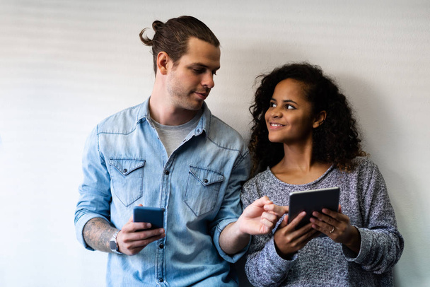 Portrait Attractive Couple in casual clothes using smartphone and digital tablet while standing over with wall. American male and African female doing online shopping together. - Foto, Bild