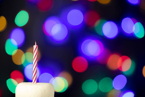 Birthday candle on a white cake with colorful lights in the background - Foto, Imagem