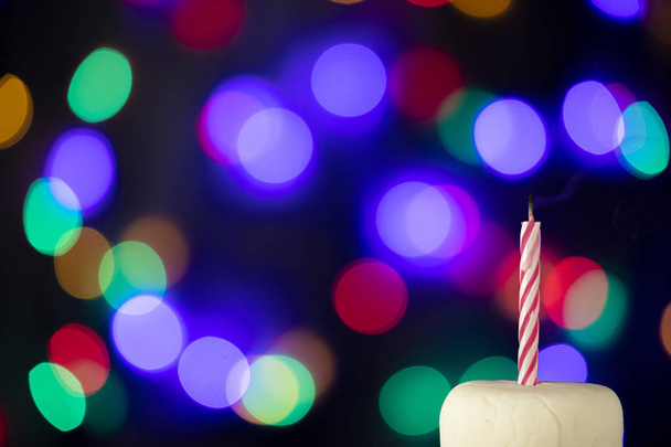 Birthday candle on a white cake with colorful lights in the background - Foto, Imagem