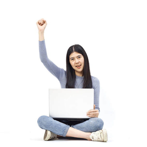 Conceito de negócio. Retrato de uma menina casual sorridente segurando computador portátil enquanto sentado em um chão e gesto feliz no fundo branco
 - Foto, Imagem