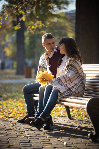Loving couple sitting and holding a bouquet of autumn leaves in the park - Photo, Image