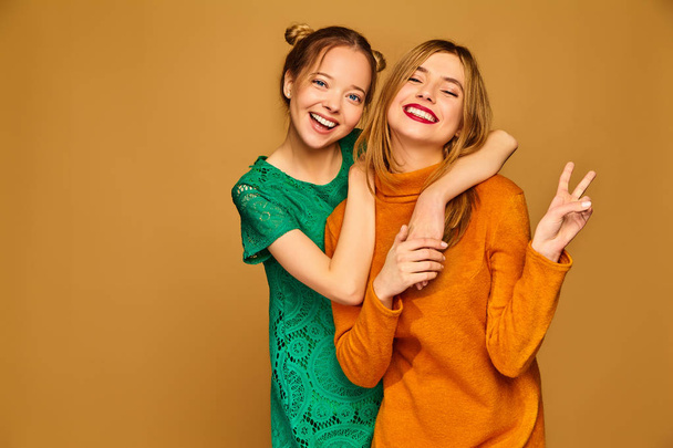Two young beautiful blond smiling hipster girls posing in trendy summer clothes. Carefree women isolated on golden background. Positive models going crazy - Foto, Bild