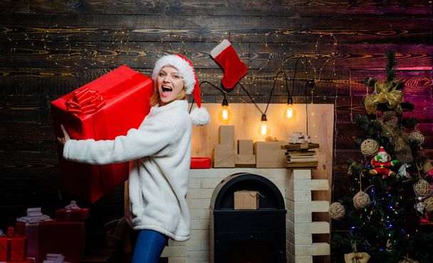 Glamour celebration new year. Blonde Santa woman holding gift box at vintage wall. Portrait of beautiful girl wearing Santa clothes. Woman in red Santa hat holding present. Woman Christmas. - Фото, зображення