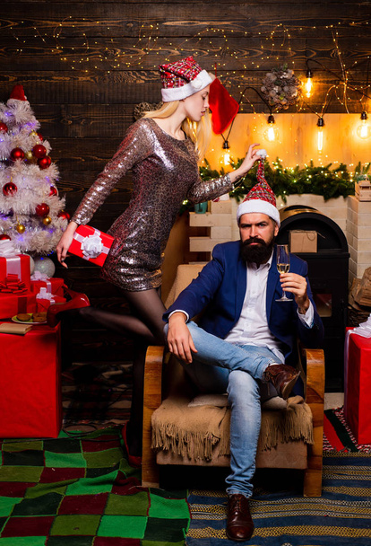 Handsome bearded hipster Santa with smiling positive young woman. Christmas tree at home. After Christmas shopping. - 写真・画像