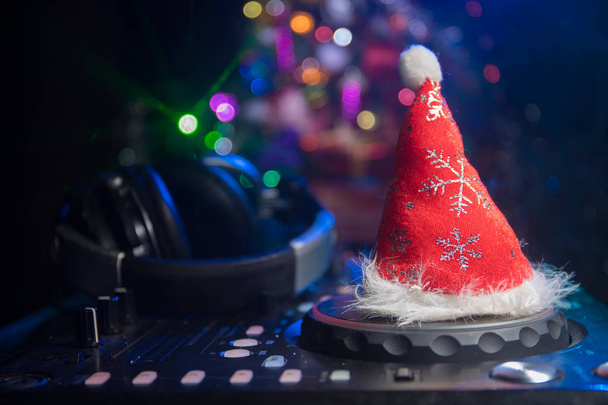 Mezclador de DJ con auriculares en el fondo oscuro club nocturno con árbol de Navidad Nochevieja. Vista de cerca de los elementos de Año Nuevo en una mesa Dj. Concepto de fiesta festiva. Espacio vacío
 - Foto, imagen