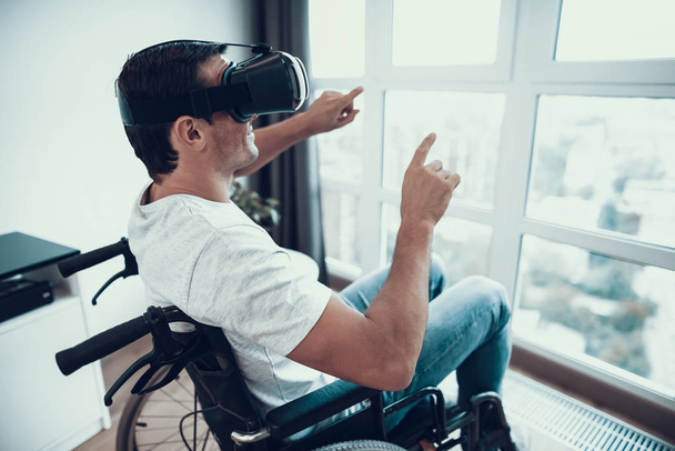 Disabled Man Enjoys VR Goggles with Hands Up. Portrait of Disabled Person Sitting in Wheelchair Parked in Large Bright Living Room. Male in Casual Clothes Pointing Finger at Window - Fotoğraf, Görsel