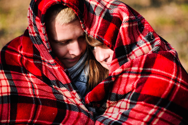 Loving para młoda ubrana w niebieski sweter siedzi z filiżanki kawy czerwony na drewno w lesie zimą - Zdjęcie, obraz