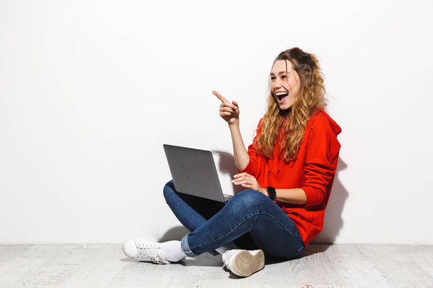 Portréja egy izgatott fiatal nő, fárasztó kapucnis ül szemben a elszigetelt fehér háttér segítségével a laptop számítógép, siker ünneplése - Fotó, kép