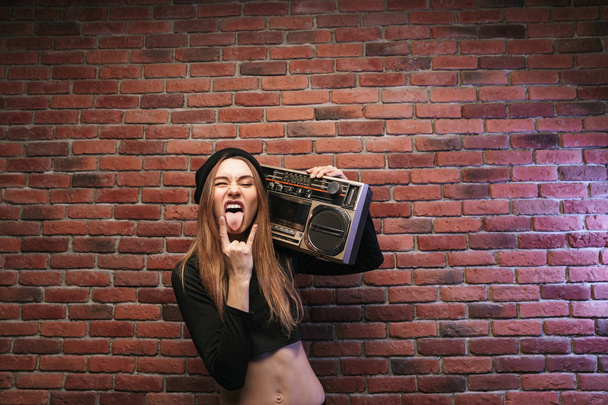 Image of cool hip hop woman 20s standing against brick wall and holding boombox - Foto, Bild