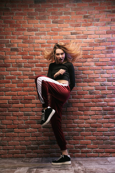 Full length photo of attractive hip hop dancer or sporty girl dancing against brick wall - Фото, зображення