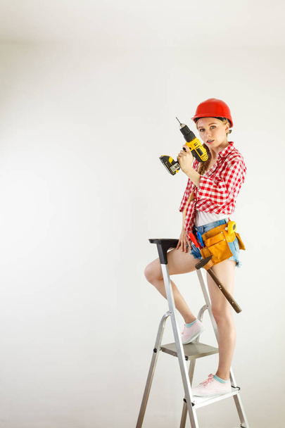 Young determinated woman using drill doing home renovation. Female construction worker having driller tool drilling wall. - 写真・画像