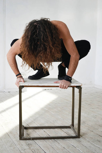 photo guy with long curly hair in a black dress sitting on a stool like a savage - Foto, imagen