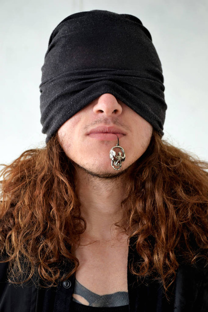 фото парень с длинными вьющимися волосами в черной одежде с повязкой на глазах держит во рту череп
 - Фото, изображение