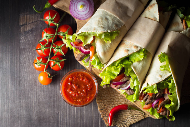 Photo of Mexican sandwich food, burrito, fajita, tacos, wrap made of tortilla, beef, chicken, fresh vegetables on rustic wooden background. Fast food concept. Healthy lunch snack. Copy space.  - Foto, Imagem