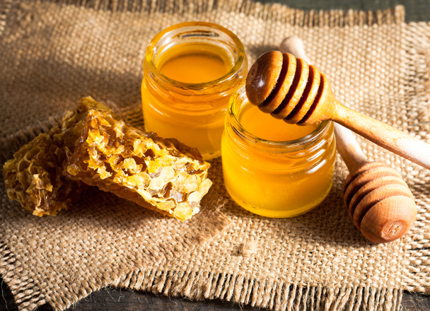 Honig tropft aus einem hölzernen Honiglöffel in einem Glas auf hölzernem grauem rustikalem Hintergrund - Foto, Bild