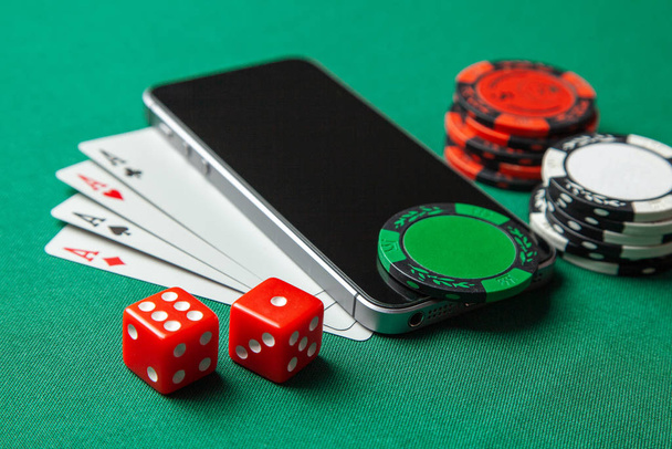 Teléfono móvil casino en línea. Teléfono móvil y tarjetas de juego con fichas y dados en una mesa de juego verde. Apuestas adicción
 - Foto, imagen