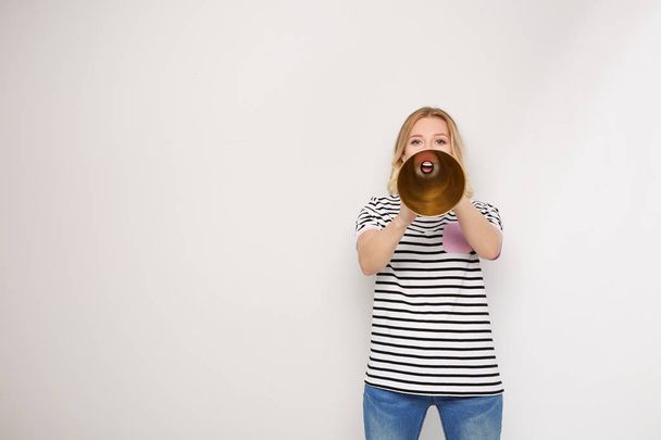 Young woman shouting into megaphone on light background. Space for text - Фото, зображення