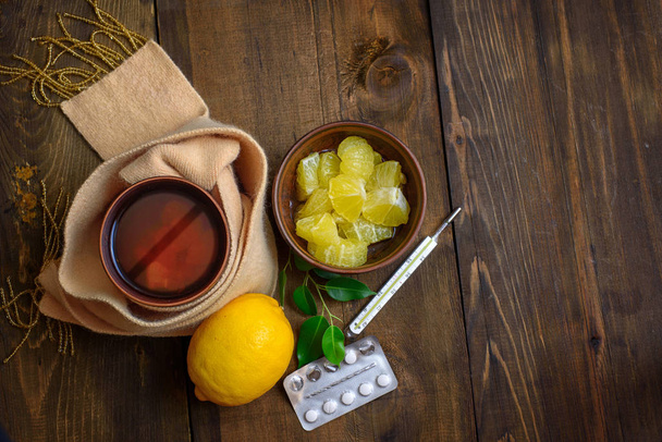 Concept illness, colds, cure, fall and winter. Tea with lemon, thermometer, pills and a knitted scarf on dark wooden background. - Fotoğraf, Görsel