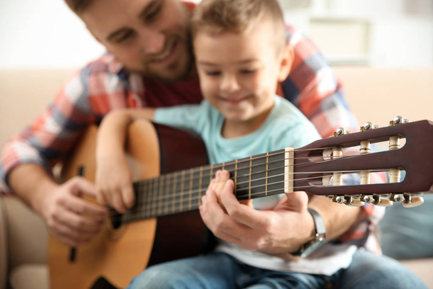 Father teaching his little son to play guitar at home - Photo, image