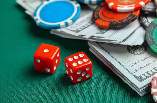 Concept de jeu au casino, poker sportif. Les dés de jeu rouges et les jetons colorés avec des dollars en espèces sur la table de jeu verte
. - Photo, image