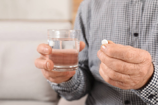 Senior man holding pill and glass of water indoors, closeup - Foto, Imagen