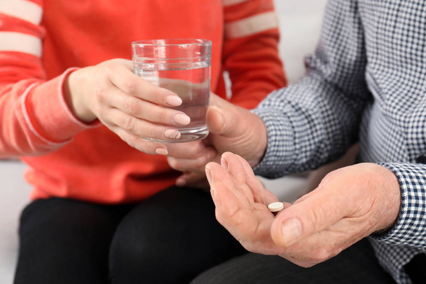 Woman giving glass of water to senior man with pill, closeup - Foto, afbeelding