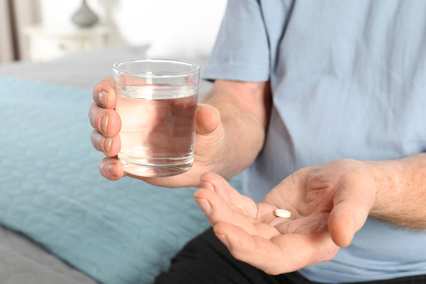 Senior man holding pill and glass of water indoors, closeup - Fotoğraf, Görsel