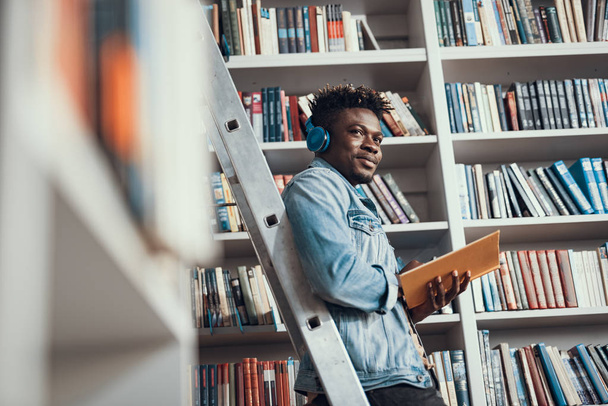 Positive student listening to music while being in the library - Photo, Image