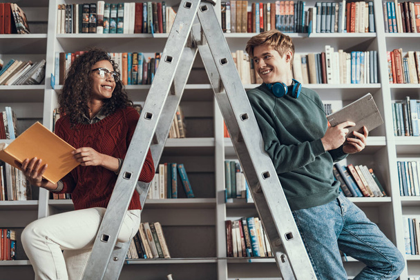 Positive friends looking at each other while sitting on step ladder - Photo, image