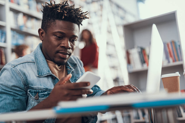 Attentive young man looking at his smartphone while studying - Photo, image