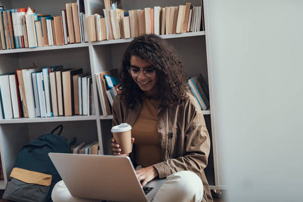 positive junge Frau schaut beim Kaffeetrinken auf den Bildschirm des Laptops - Foto, Bild