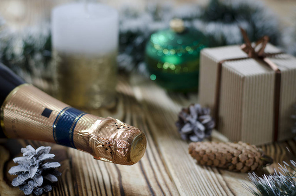 Рождественская открытка: Подарок лежит на деревянном столе рядом со свечой, шишками и ангелом на фоне рождественских украшений
. - Фото, изображение