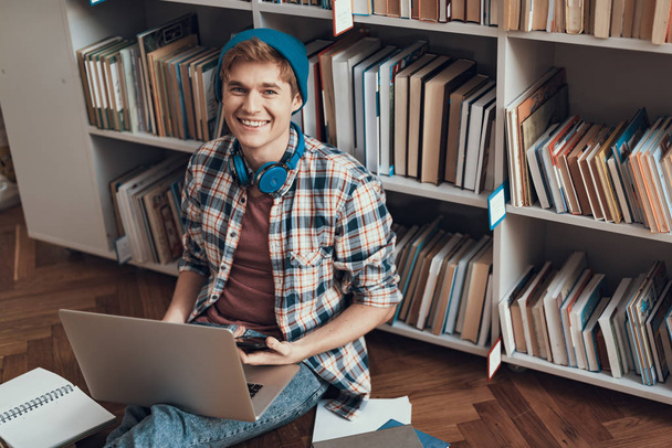 Waist up of positive student sitting on the floor with laptop - Фото, изображение